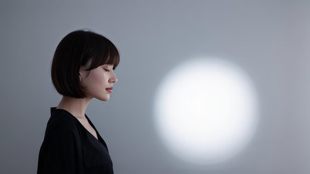 The photograph features a young Asian woman with dark hair styled in a bob cut wearing an elegant black outfit. She is seen from behind gazing into the distance against a gradientの素材