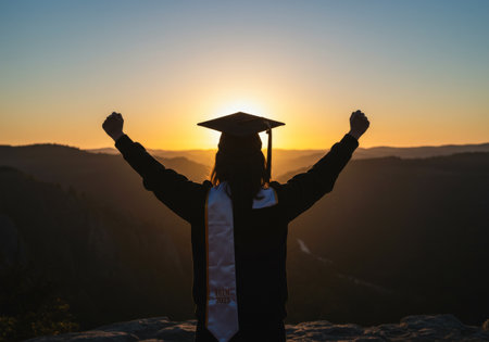 A graduation day celebration with students raising their arms in joyous triumph atop a majestic mountain peakの素材