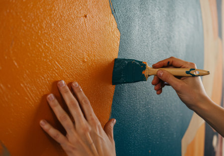 A person skillfully applies green paint on an orange and blue wall with vibrant colors blending harmoniouslyの素材