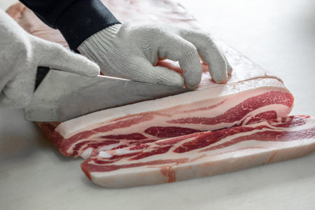 Butcher cutting a piece of bacon on a marble countertop.