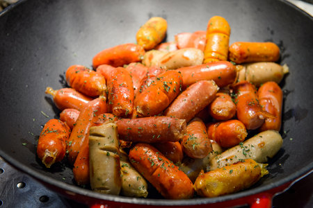 Fried sausages in a frying pan with spices and herbsの写真素材