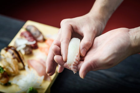 Close-up of male hands preparing sushi on wooden table in restaurantの写真素材