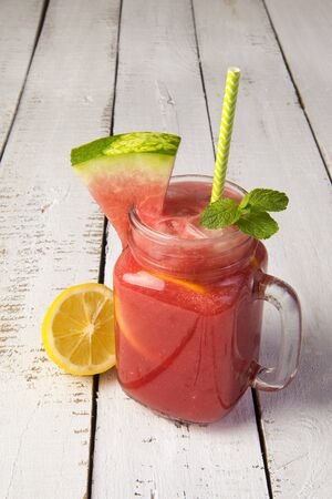 Refreshing watermelon lemonade with lemon and mint in a glass jar on a white wooden tableの写真素材