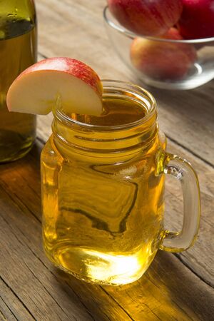 A glass jar of cold apple cider on an old rustic wooden table with a glass bottle and ripe red apples. Selected focus.の写真素材
