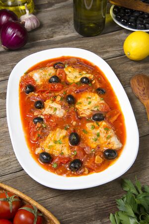 Pan seared fish with tomatoes and olives on an old rustic wooden table. Selected focus.の写真素材