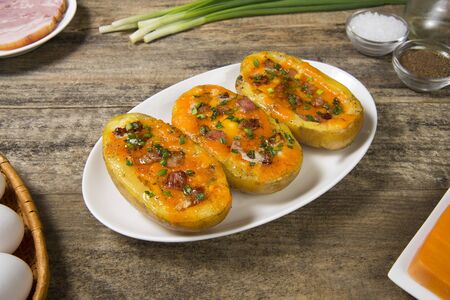 Potato stuffed with ham and egg, baked with cheese with ingredients on a rural wooden table. Selected focus.の写真素材
