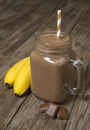 Chocolate banana smoothie in a glass jar with ingredients on a rustic wooden table. Selected focus.の写真素材