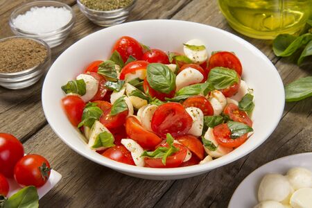 Traditional caprese salad on a rustic wooden table with ingredients. Selected focus.の写真素材