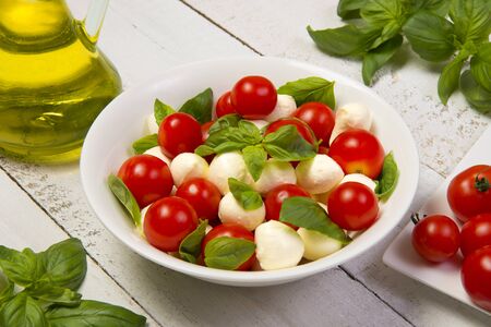 Caprese salad in a round white salad bowl on an white wooden table. Selected focus.の写真素材