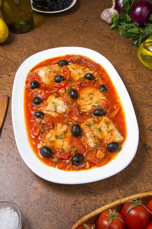 Pan seared fish with tomatoes and olives on an brown table.の写真素材