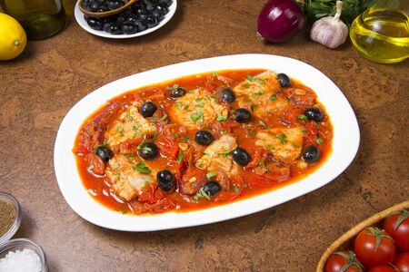 Pan seared fish with tomatoes and olives on an brown table.の写真素材