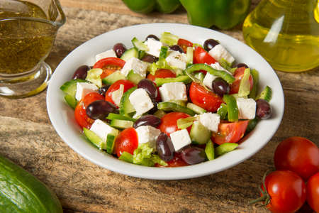 Greek salad in a round white bowl on an old rustic wooden table. Selected focusの写真素材