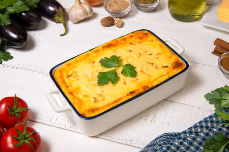 Greek Moussaka close up in casserole dish with the ingredients on the white rustic table.の写真素材