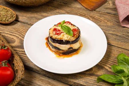 Baked eggplant and tomatoes mozzarella and parmesan stacks with ingredients on a rustic wooden table. Close up. Selected focus.の写真素材