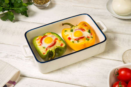 Bell peppers stuffed with vegetables, baked with cheese and quail eggs in a casserole on a white rustic table.の写真素材