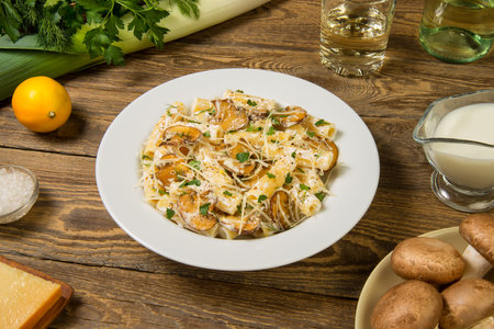 Pasta with mushrooms, white wine and leeks in white plate on a rustic table along with the ingredients. Close up.の写真素材