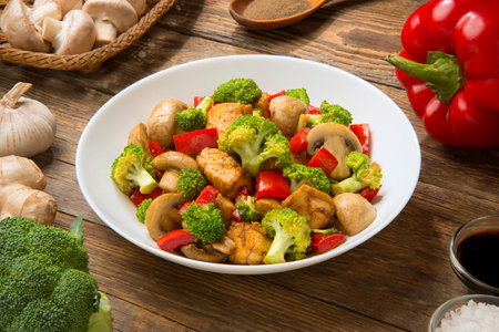 Keto low carb chicken stir fry with bell peppers, mushrooms, ginger and broccoli in a salad bowl on a wooden rustic table.の写真素材