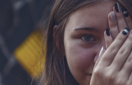 a girl covering her left eye with both hands as she tries to see the right eye in the dim light. The...