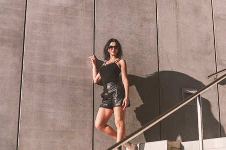 Dark-haired woman posing in a black dress on the concrete stairs. The woman is wearing black...