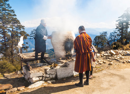 Dochula Pass/ Bhutan - March 01, 2016: tThree Bhutanese men in traditional Bhutanese clothes perform a religious ceremony of ignition on the Dochula Pass, Himalayaのeditorial素材