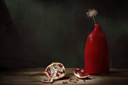 Classic still life with pomegranate fruit and red vase on dark background. Art photographyの写真素材