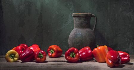 Still life with red bell paprika and a large antique jug on the background of a cracked wallの写真素材