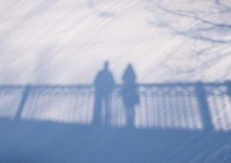 Shadow silhouette of couple man and woman standing on a bridge on snow background on sunny winter...