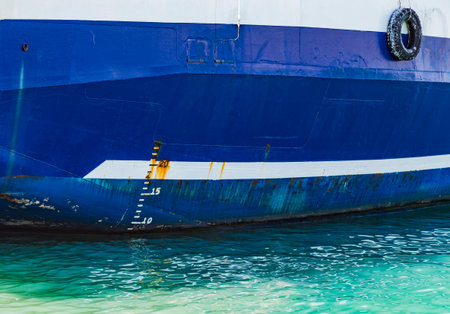 Side of blue cargo ship hull with white waterline and numbers of rough draft scale. International...