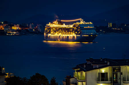 Saranda, Albania - September 2019: Big cruise ship MSC Musica with festive night lights stopped for the night in the bay near the sea port of Saranda. Albanian mountains and Saranda town in the background.のeditorial素材