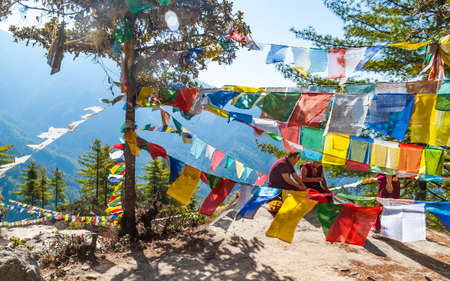Paro, Bhutan - February 2016: buddhist monk in traditional red clothes and multicolor prayer Tibetan Buddhist flags Lung Ta in Himalayas on the way to Taktsang Monastery or Tiger's Nestのeditorial素材