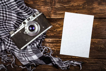 Old retro camera on vintage brown wooden board with black and white checkered scarf and piece of squared paper for notes. abstract background. Top view.Copy space for text.の写真素材