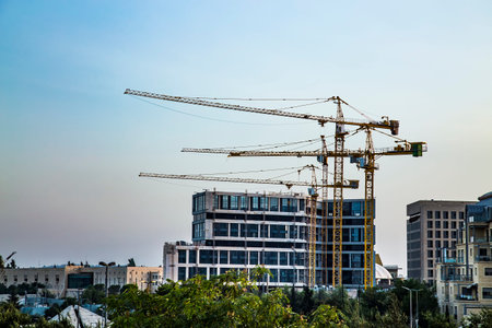 Big building cranes on the background of modern building under construction in twilight.