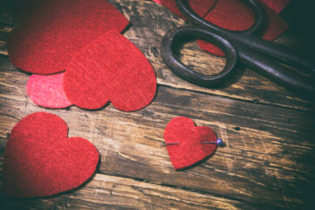 A lot of handmade felt hearts, one pierced with a pin and vintage scissors on a wooden board. Vintage style. Valentine's Day concept. Top view.の写真素材