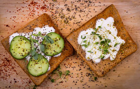 Healthy sandwiches with cream cheese, pea and linen microgreens, cucumber slices and spices on cutting board. Healthy eating, diet vegan food. Top view.の写真素材