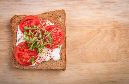 Healthy sandwich with cream cheese, microgreens and tomato slices and spices on cutting board. Healthy eating, diet vegan food. Top view.の写真素材