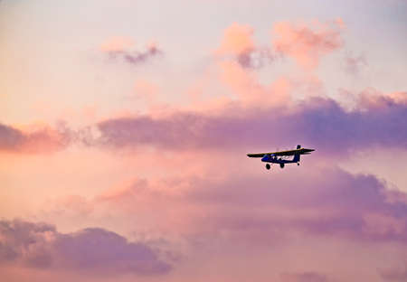 silhouette of ultralight microlite aircraft flying with a pilot and a passenger against sunset sky.の写真素材
