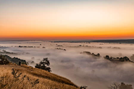 Beautiful panoramic landscape with river valley covered by thick fog in autumn in the early morning. Sunrise.の写真素材
