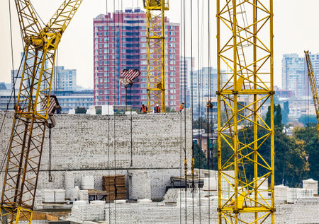 Bricklayer workers in safety orange vests and hard hats make walls of white silicate bricks on a...