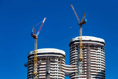 Tel Aviv, Israel - 29 of July 2019: Two building crane attached to the construction of a modern high-rise building at the background of bright blue sky, high-rise building.のeditorial素材