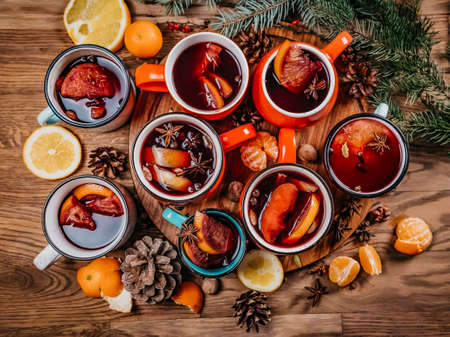 Top view of many colorful cups of traditional Christmas drink mulled red spiced wine with cinnamon stick, apples and citrus on wooden table with star anise and christmas fir tree. Christmas party.の写真素材
