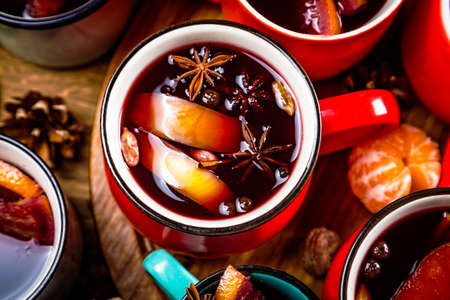 Close up top view of colorful cups of traditional Christmas drink mulled red spiced wine with cinnamon stick, apples and citrus on wooden table with star anise and christmas fir tree. Christmas party.の写真素材