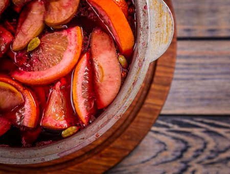 Big kettle pot of traditional hot steaming Christmas drink mulled red spiced wine gluhwein boiling with apples and citrus on wooden background. Christmas party.の写真素材