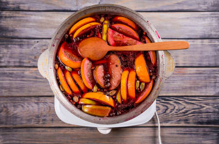 Big kettle pot of traditional hot steaming Christmas drink mulled red spiced wine boiling with apples and citrus with wooden spoon on black background. Christmas party.の写真素材