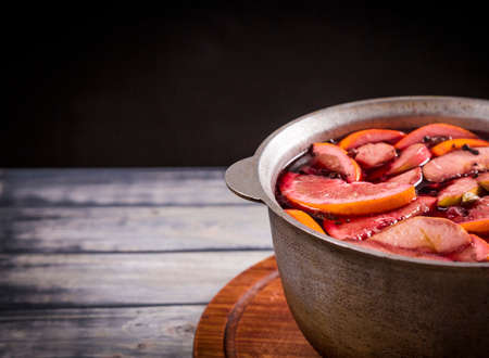 Big kettle pot of traditional hot steaming Christmas drink mulled red spiced wine boiling with apples and citrus on black background. Christmas party.の写真素材