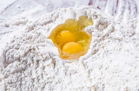 Baking scenery with a heap of wheat white flour for kneading dough for pasta or pizza with a raw egg on top. Close up. Homemade baking concept.の写真素材