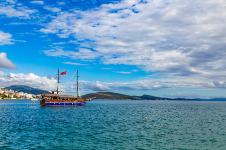 Saranda, Albania - September 2019: Vintage mast wooden sailing ship Onhesmus for sea tours in port of Saranda, Albania on the background of Saranda town. Cloudy day. Sea landscape.のeditorial素材