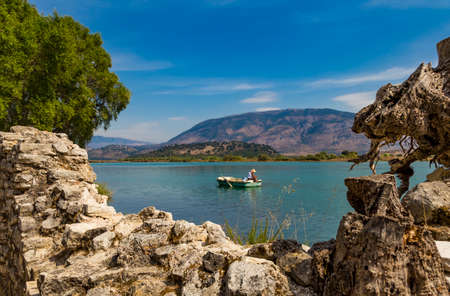 An albanian fisherman in his boat on Butrint lake salt lagoon, view from Butrint National Park, in Albania, archeological site in Ksamil.の写真素材