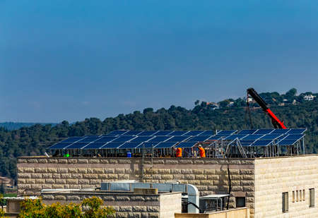 Installation of solar cell electric panels on a roof of multi-storey building in Israel. Solar panels on the house roof. Workers are installing the solar cell farm power plant. eco technology.の写真素材