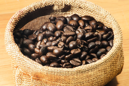 coffee beans in coffee bag made from burlap on wooden surface.の写真素材