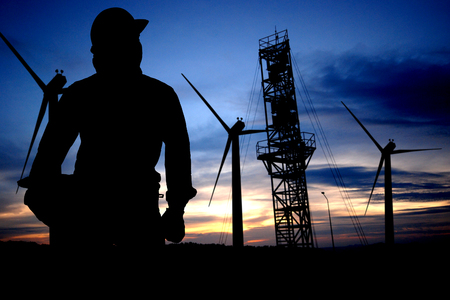 The silhouette of an engineer standing at a power station and wind turbine towersの写真素材